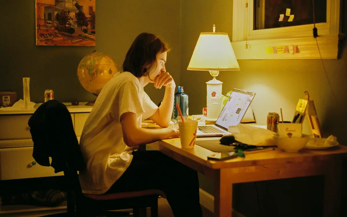 Opositora estudiando de noche en su escritorio, iluminada por una lámpara, con el portátil abierto